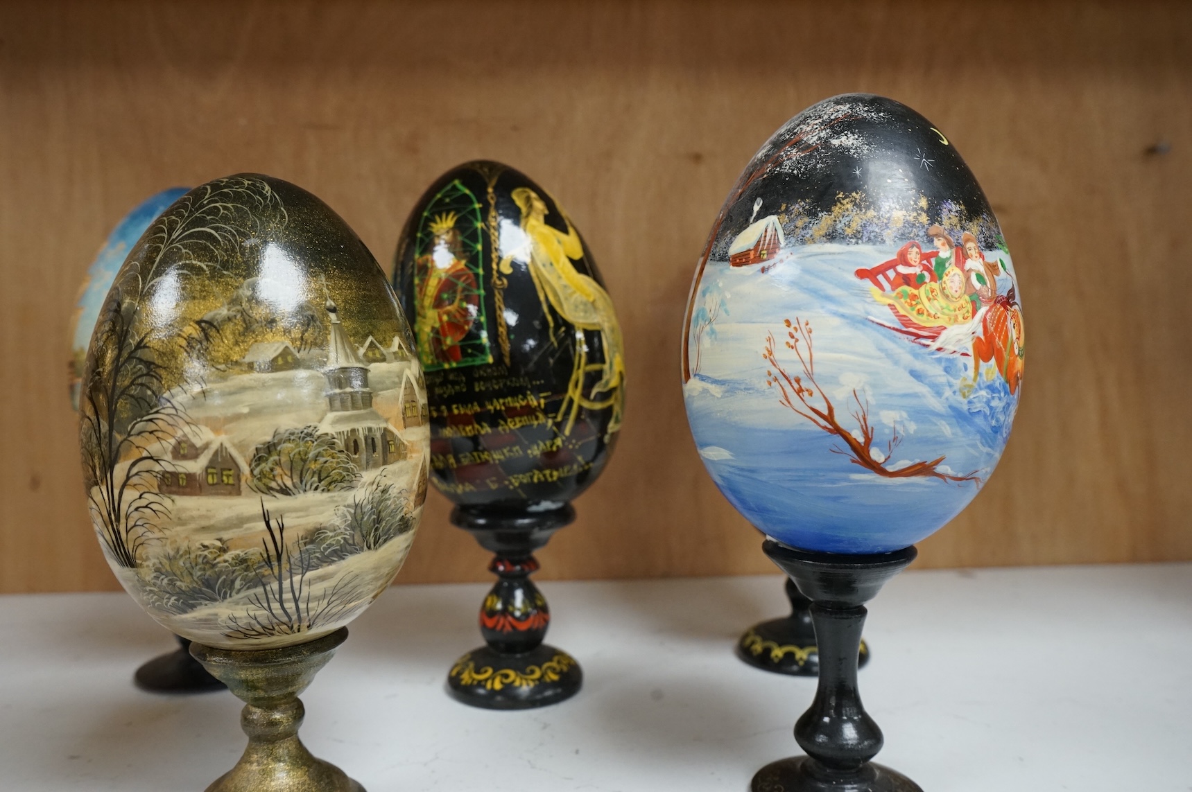 Five Russian painted and lacquered 'eggs' on stands, one inscribed in cyrillic, largest 21cm high